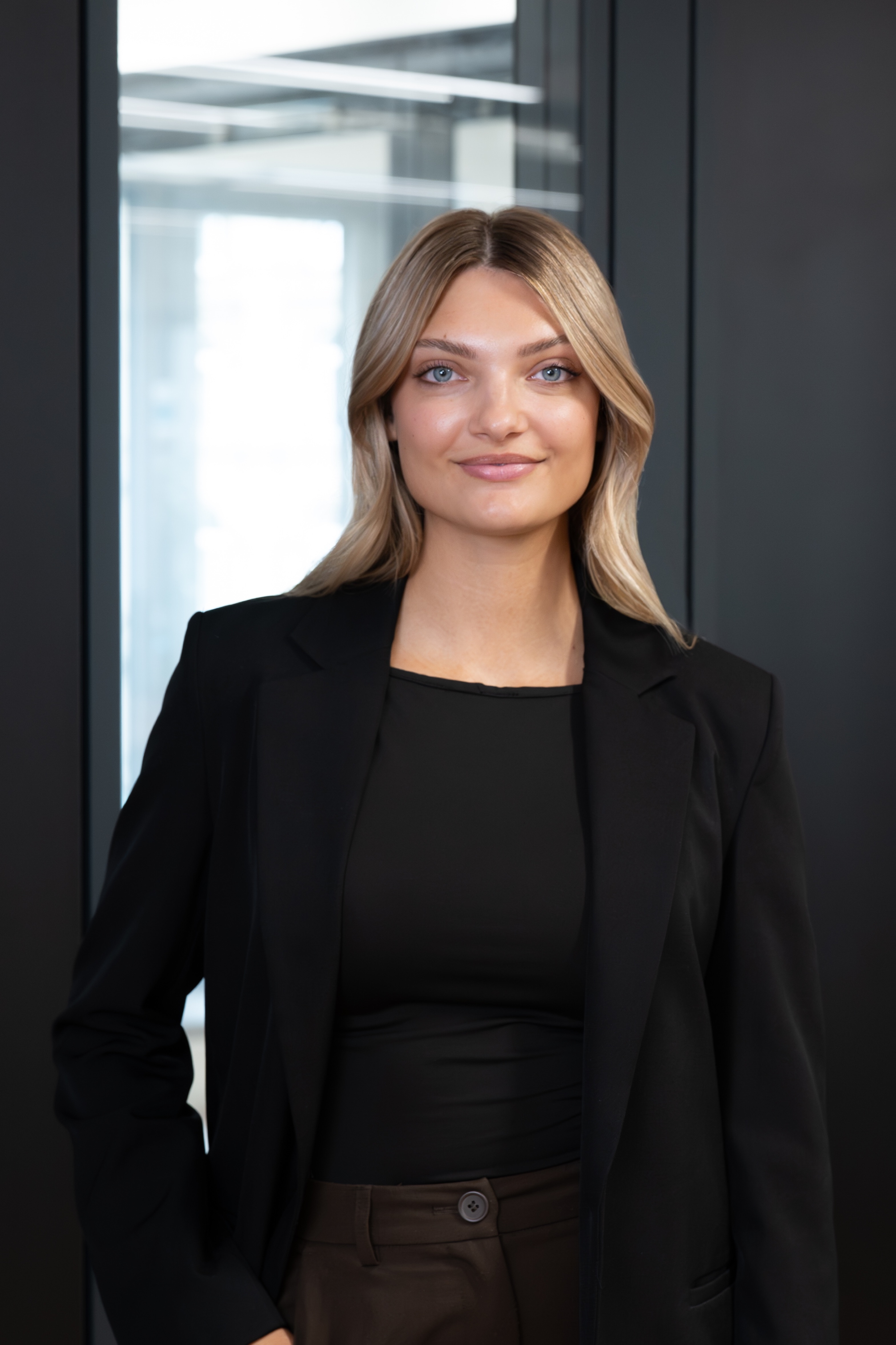 Junge Frau mit langen blonden Haaren steht in einem modernen Raum mit Glaswand.