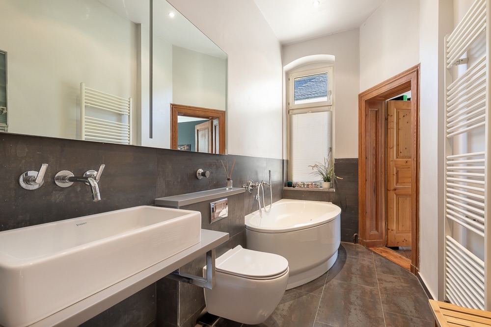 Modernes Badezimmer mit Eckbadewanne, großem Spiegel, Waschbecken und Wandheizkörper.