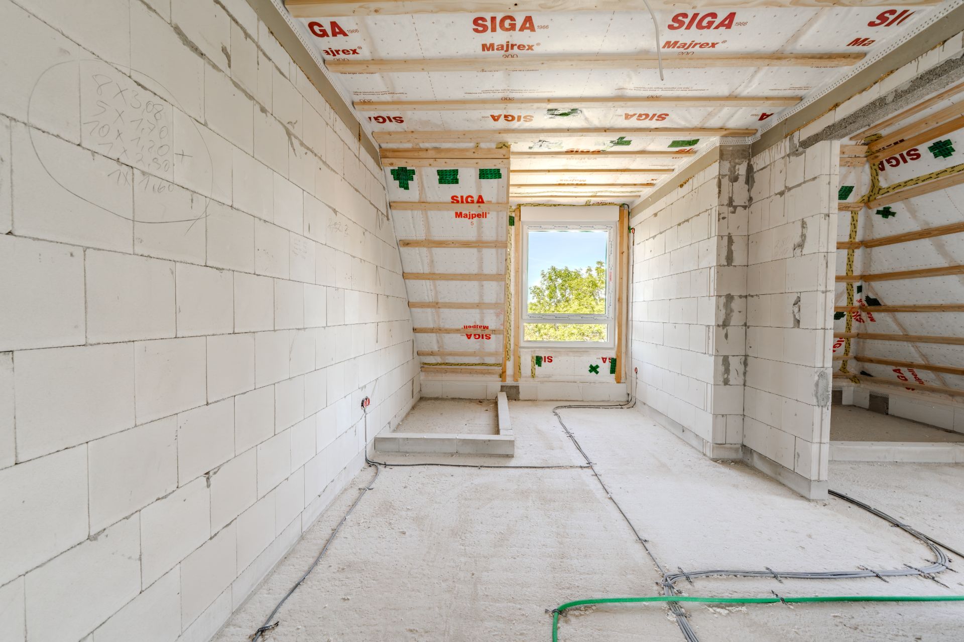 Unfertiger Raum mit weißen Wänden, Decke in Bau, Fenster mit Blick auf Bäume.