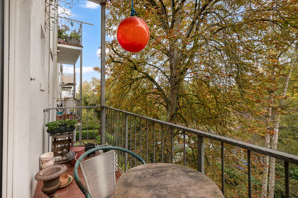 Balkon mit Tisch, Stühlen und Pflanzgefäßen, Ausblick auf einen großen Baum.