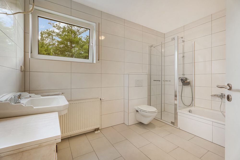 Modernes Badezimmer mit Fenster, Dusche, Badewanne, Waschbecken und Wandtoilette.