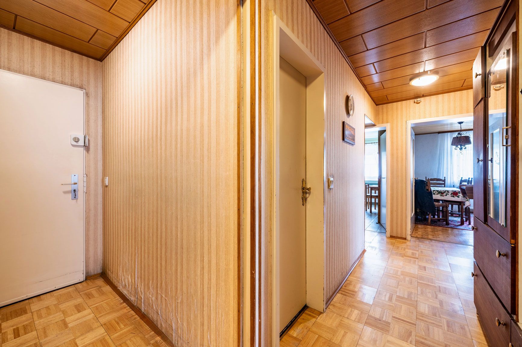Heller Flur mit Holzboden, Holzwanddecke und Zugang zu mehreren Zimmern, sichtbar Esszimmer im Hintergrund.