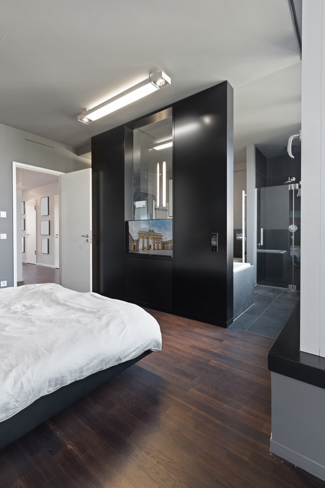 Modernes Schlafzimmer mit dunklem Holzboden, Bett und offenem Zugang zum Bad.