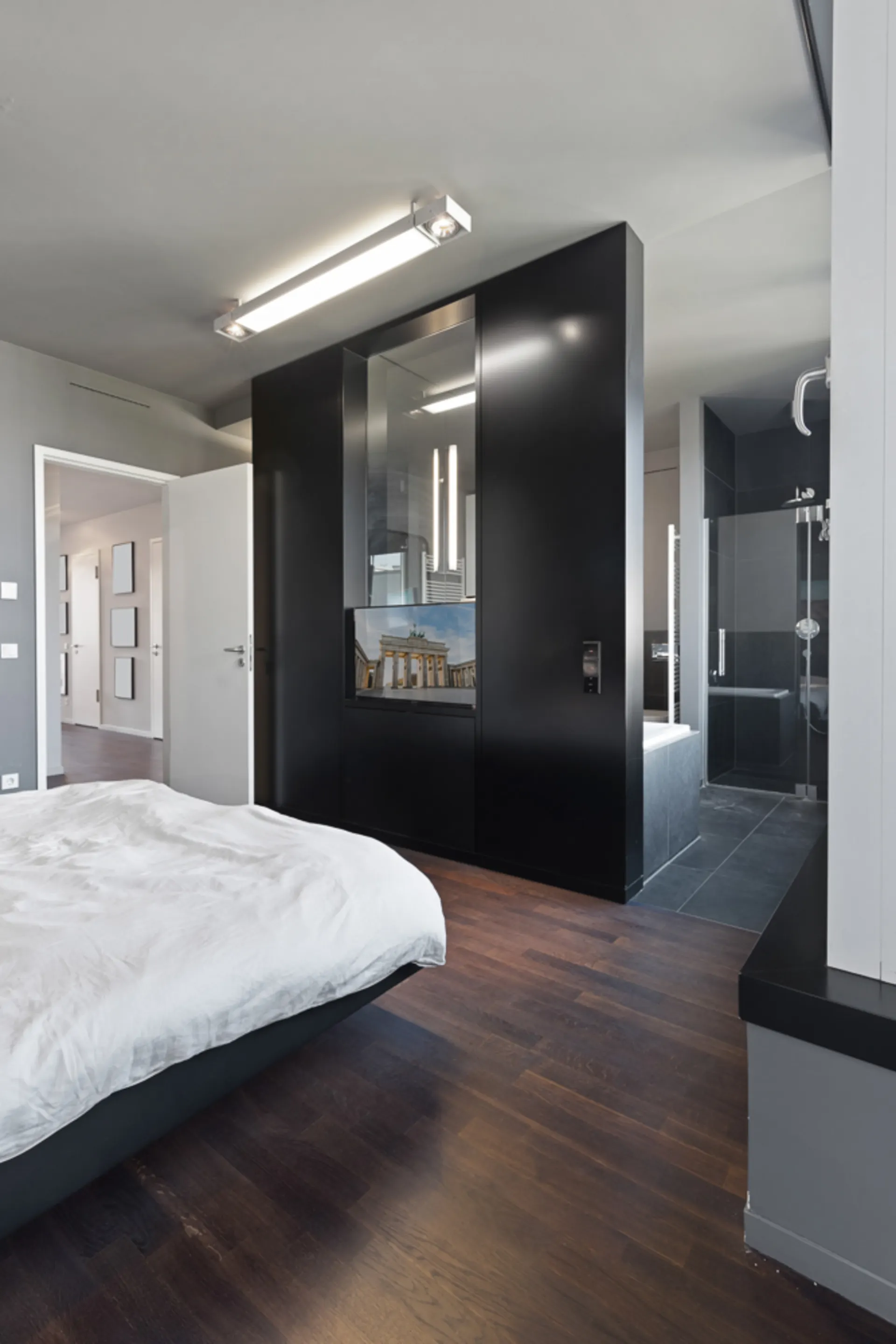 Modernes Schlafzimmer mit dunklem Holzboden, Bett und offenem Zugang zum Bad.