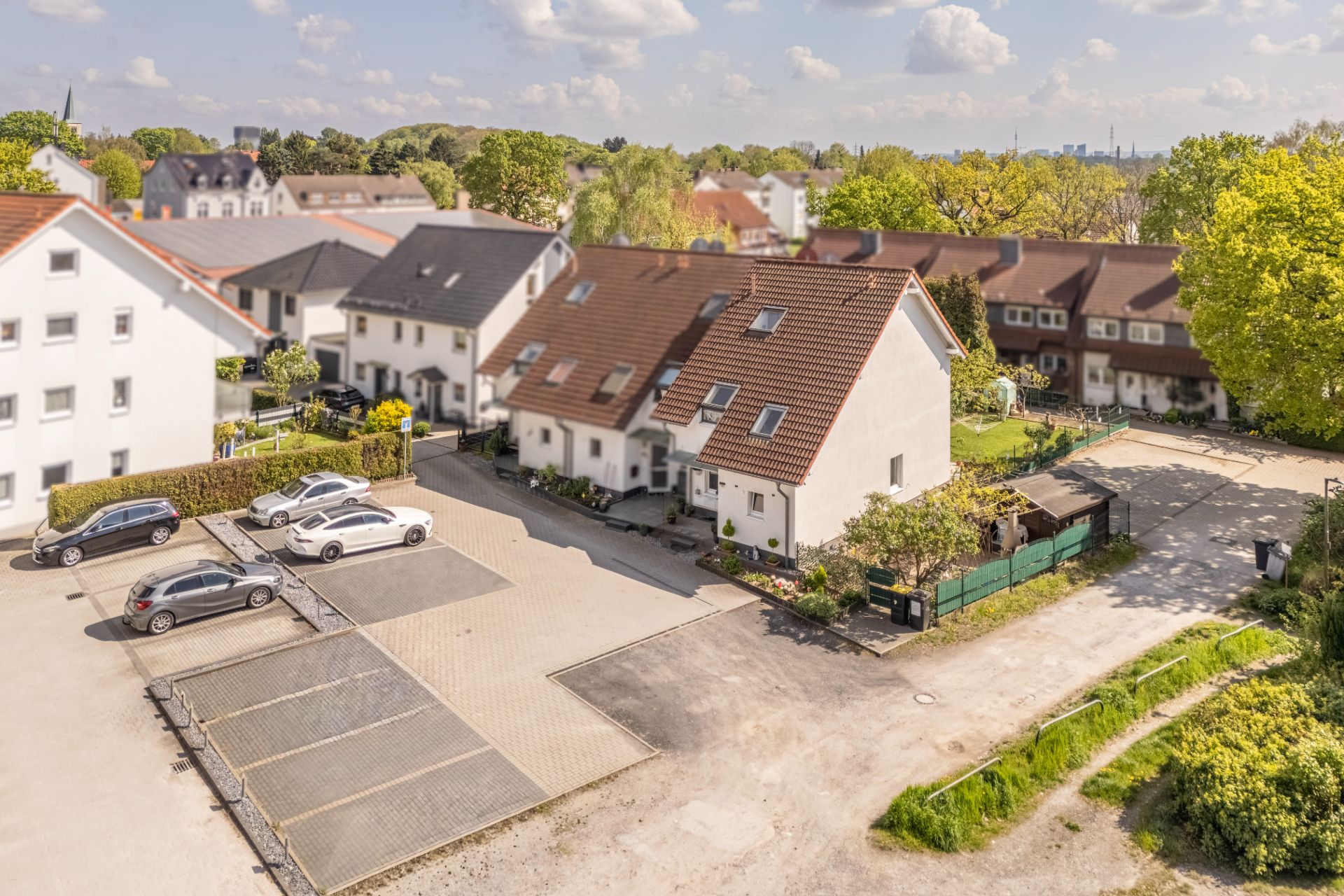 Mehrere Reihenhäuser mit roten Dächern, Parkplätze und Grünflächen bei sonnigem Wetter.