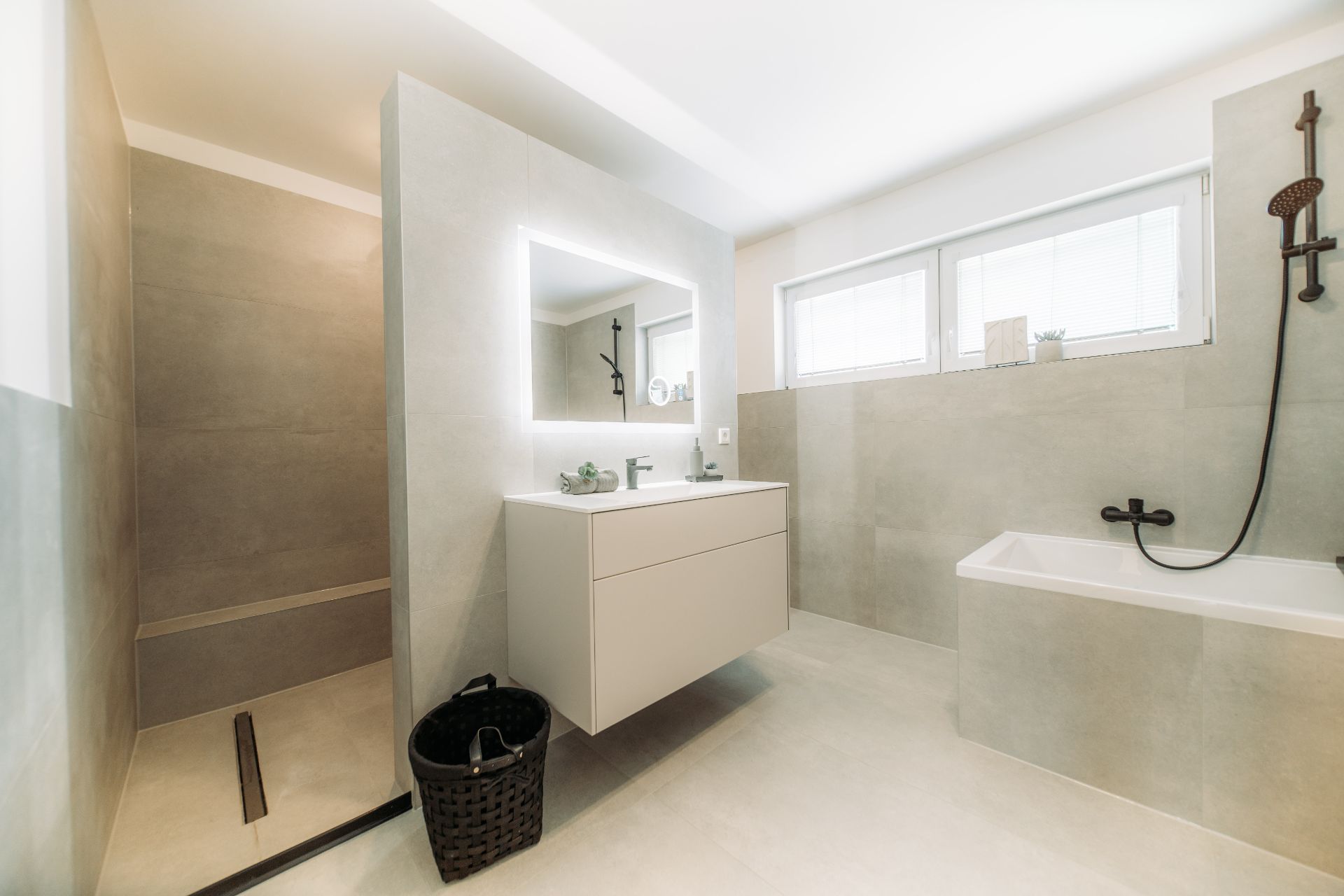 Modernes Badezimmer mit Dusche, Badewanne, beleuchtetem Spiegel und Waschbecken.