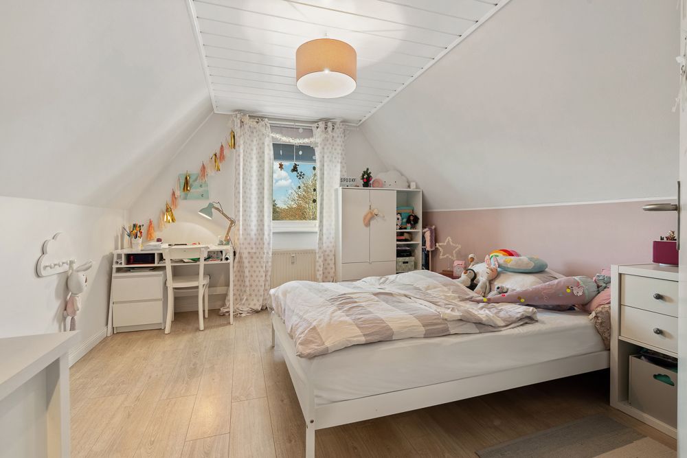 Kinderzimmer mit Bett, Schreibtisch, weißen Möbeln und Dachschräge.