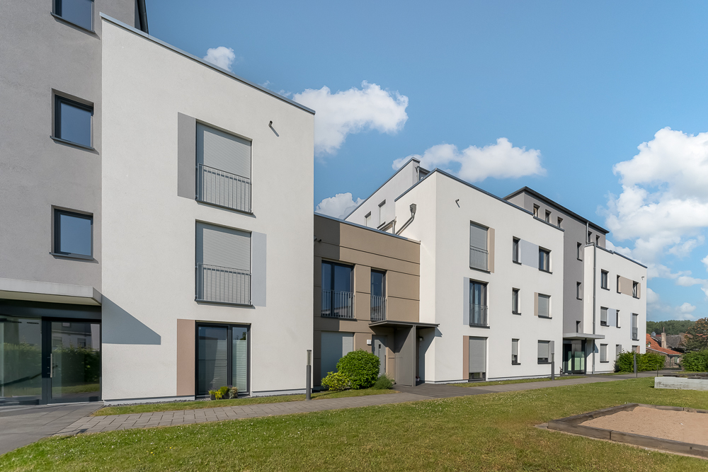 Moderne Wohngebäude mit mehreren Stockwerken und Rasenfläche im Vordergrund.