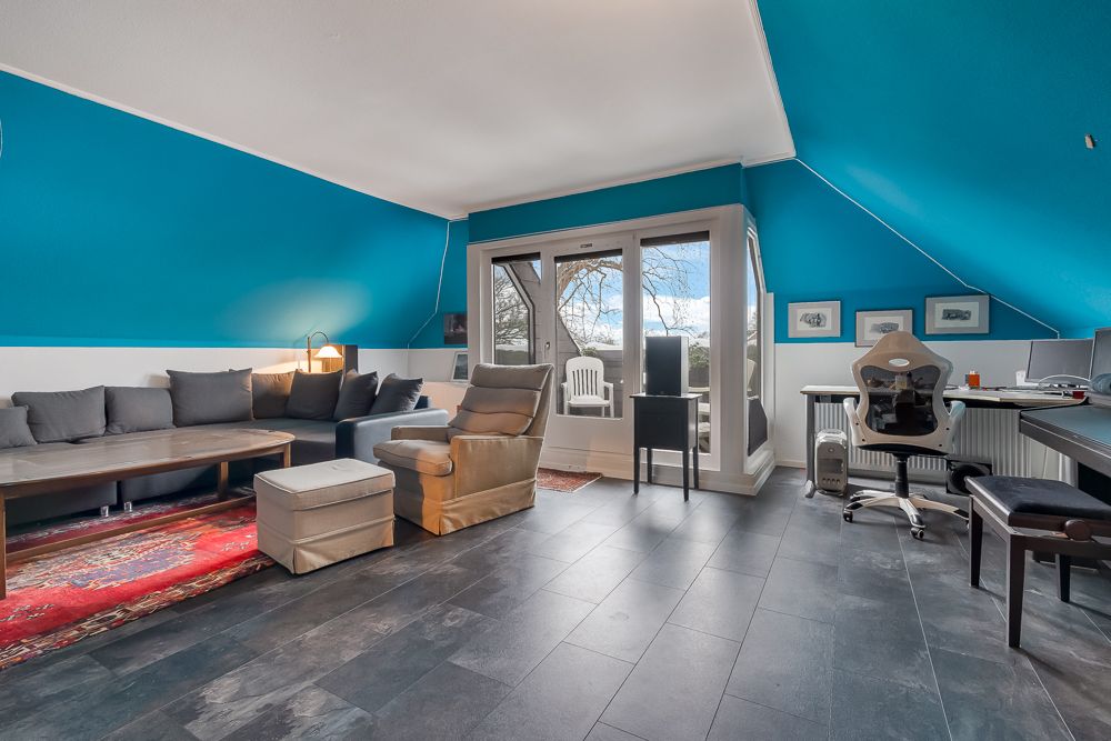 Wohnzimmer mit Ecksofa, Sessel, Schreibtisch und Zugang zum Balkon, blaue Wände.