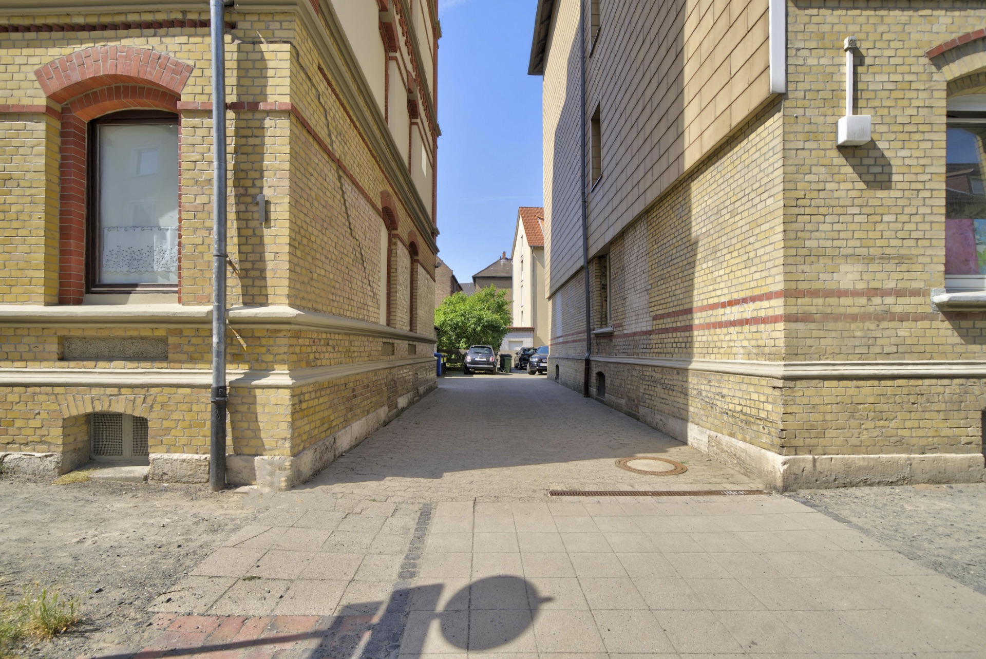 Gepflasterter Weg zwischen zwei gelben Backsteingebäuden mit sichtbaren Fenstern.