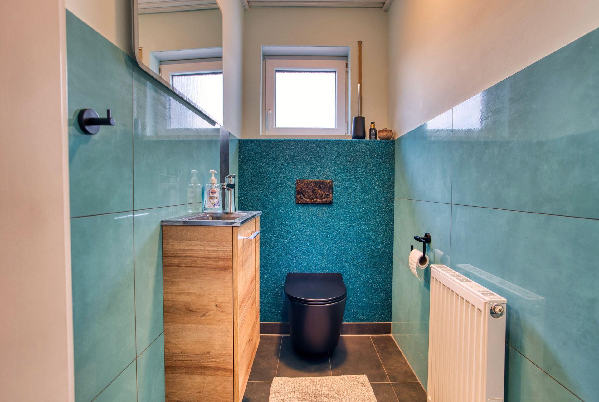 Modernes Badezimmer mit schwarzer Toilette, Holzwaschtisch, grün-blauen Fliesen und Fenster.