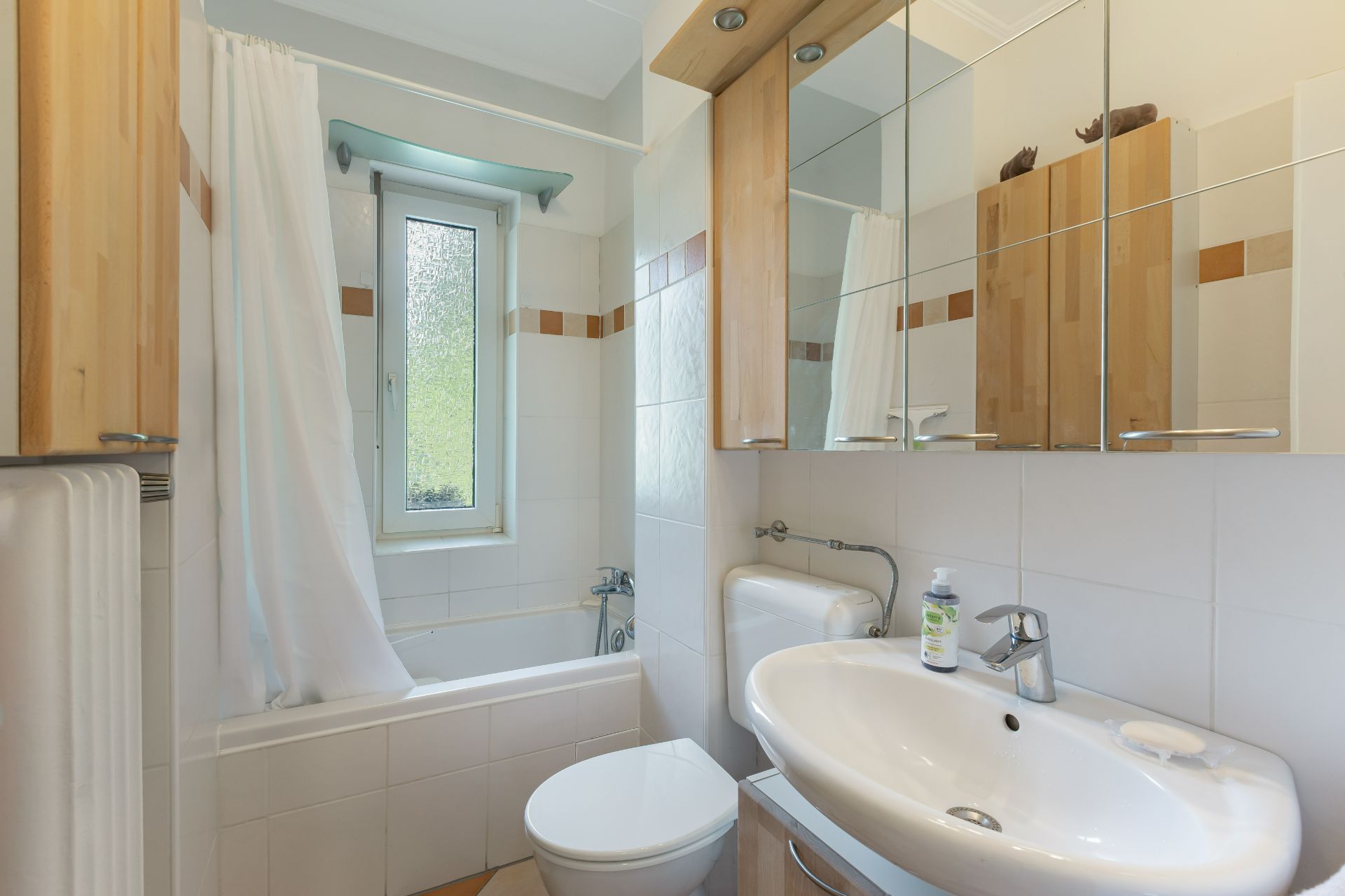 Helles Badezimmer mit Badewanne, Duschvorhang, Waschbecken, Toilette und Spiegelschrank.