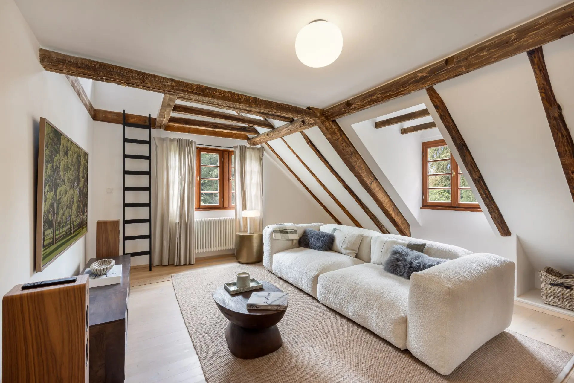 Wohnzimmer mit Holzbalken, weißem Sofa, Couchtisch und Fenstern mit Vorhängen.