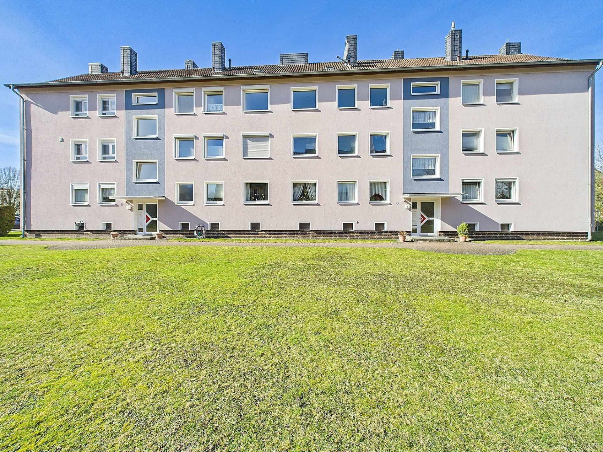 Dreistöckiges Wohnhaus mit vielen Fenstern und großer Rasenfläche davor.