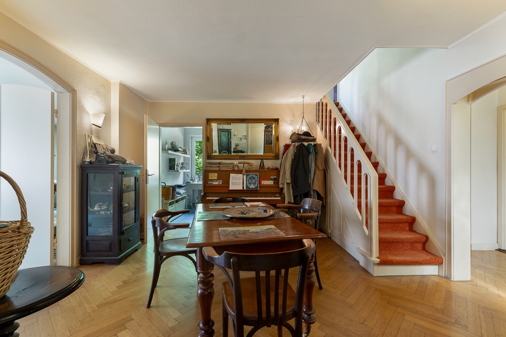 Esszimmer mit Holztisch, Stühlen und roter Treppe, Spiegel an der Wand.