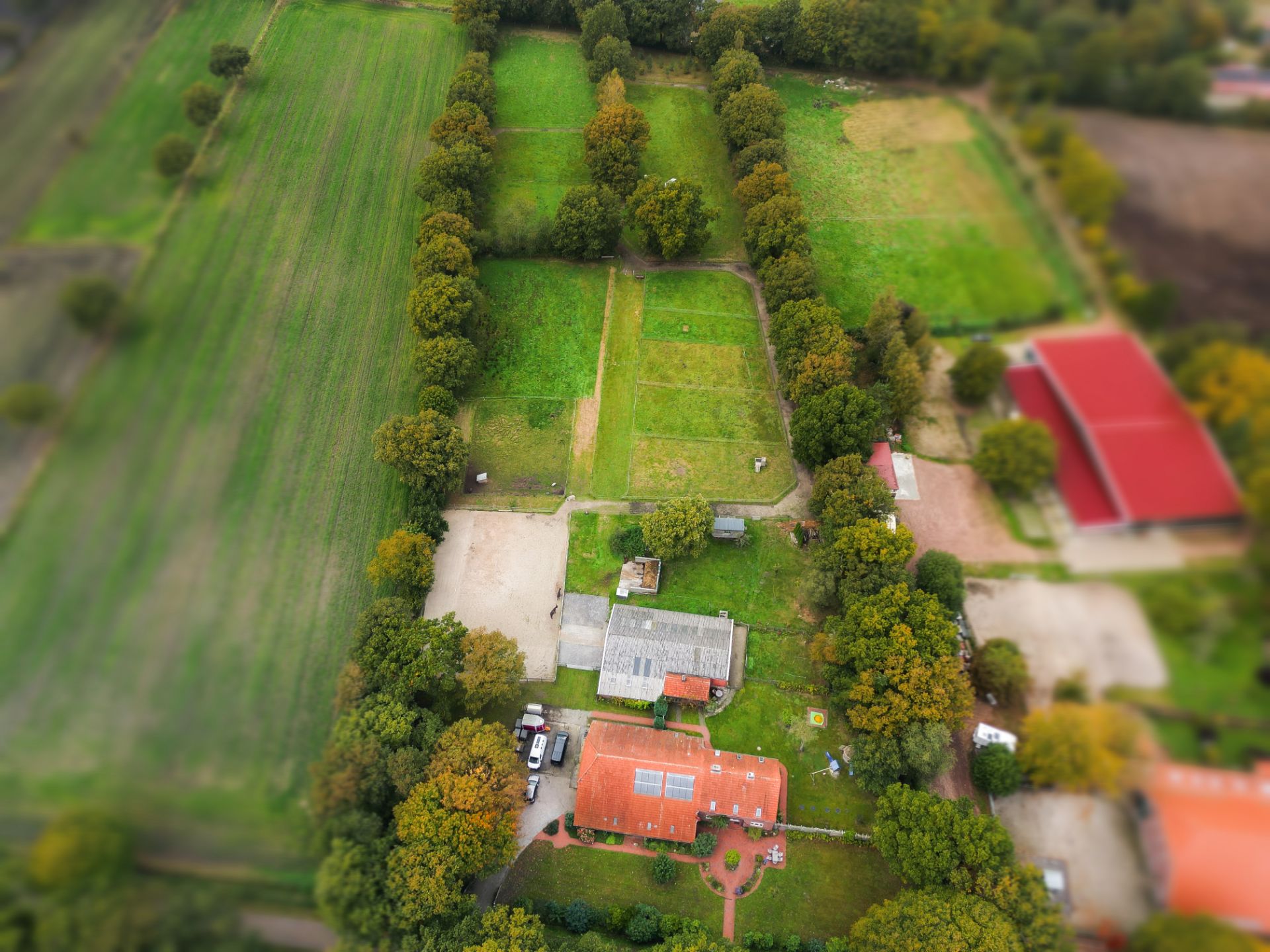 Luftaufnahme eines Wohnhauses mit Nebengebäuden und großen, von Bäumen gesäumten Wiesen.
