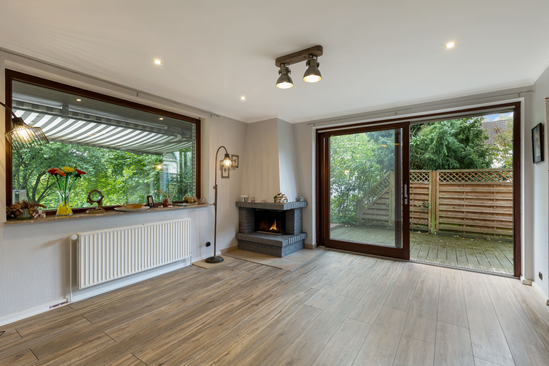 Helles Wohnzimmer mit Kamin, großem Fenster, Terrassentür und Holzboden.