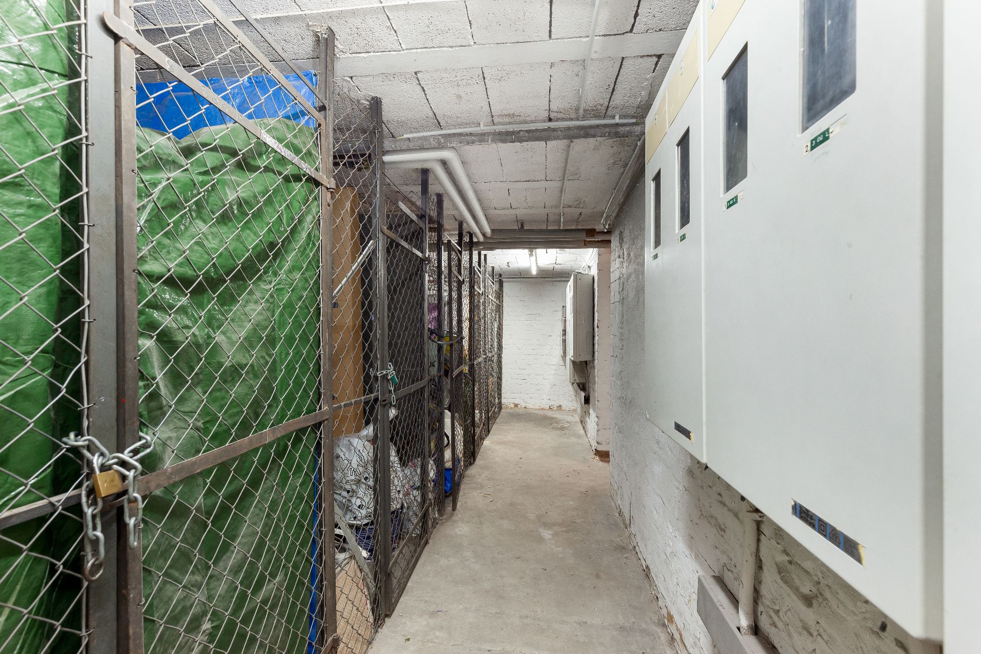 Kellergang mit abgeschlossenen Metallgitter-Abteilen und weißen Verteilerkästen an der Wand.
