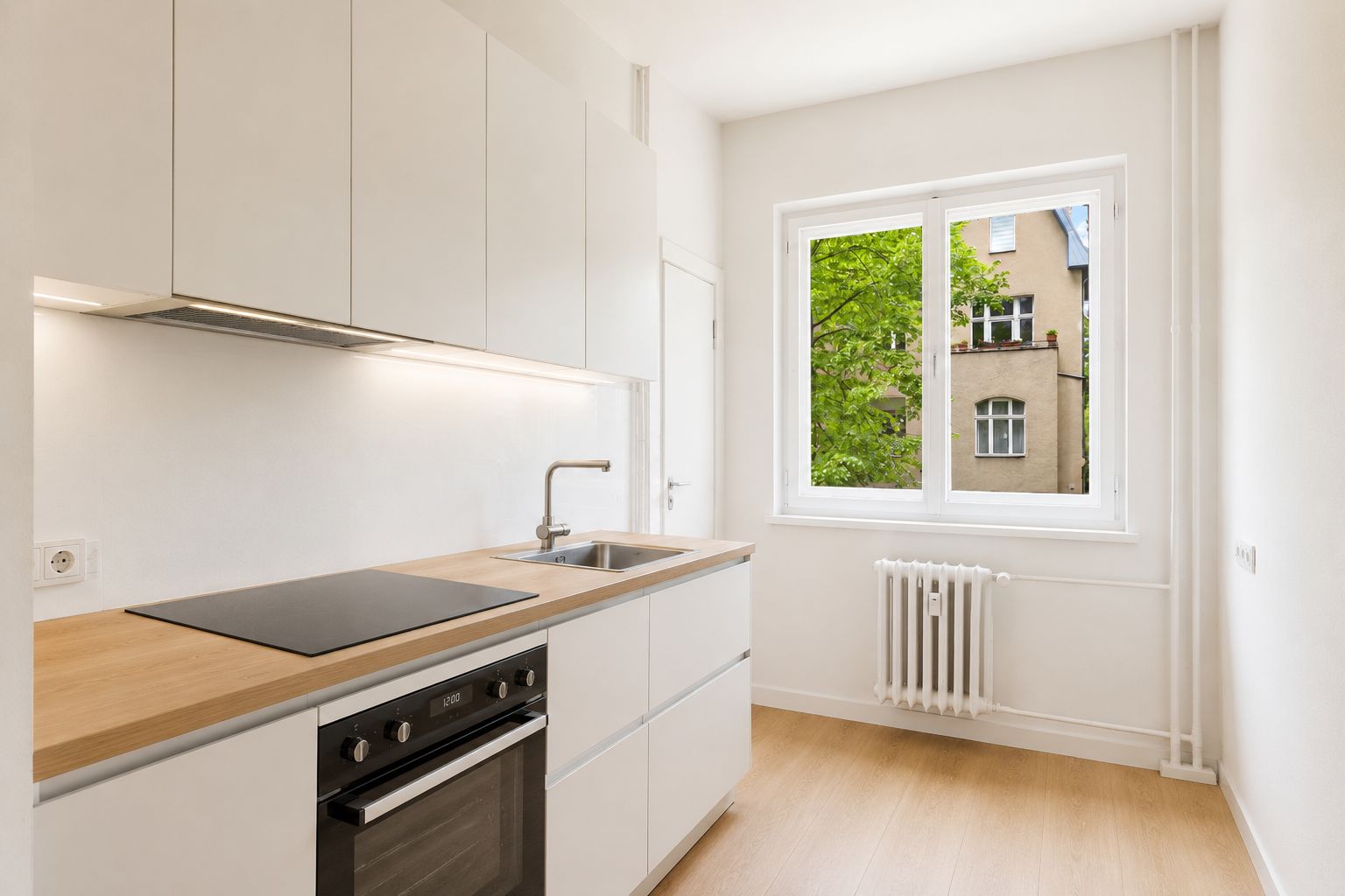 Helle, moderne Küche mit Herd, Spüle, weißen Schränken und Fenster mit Blick nach draußen.