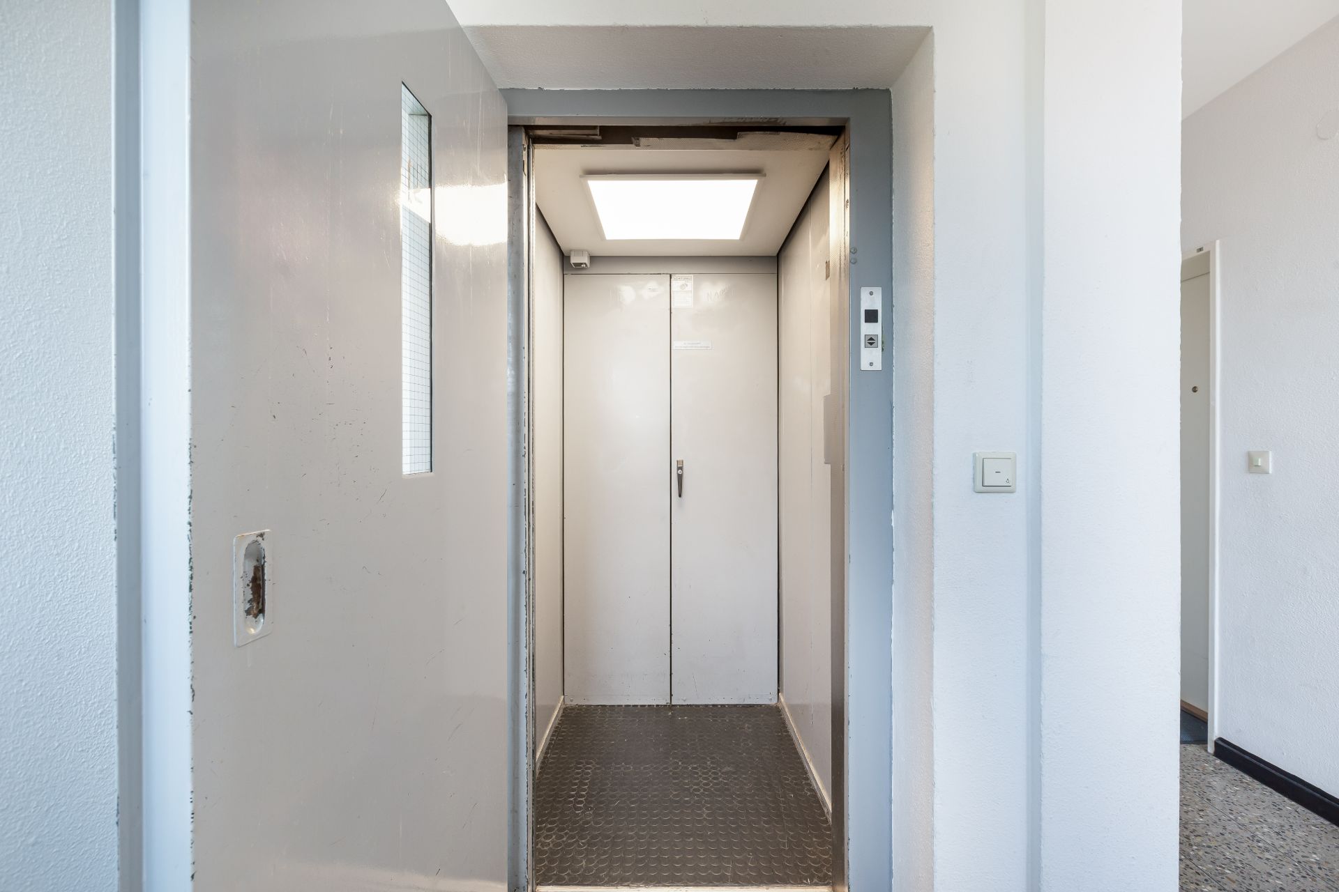 Offener Aufzug mit geschlossener Tür und beleuchtetem Innenraum in einem Wohngebäude.