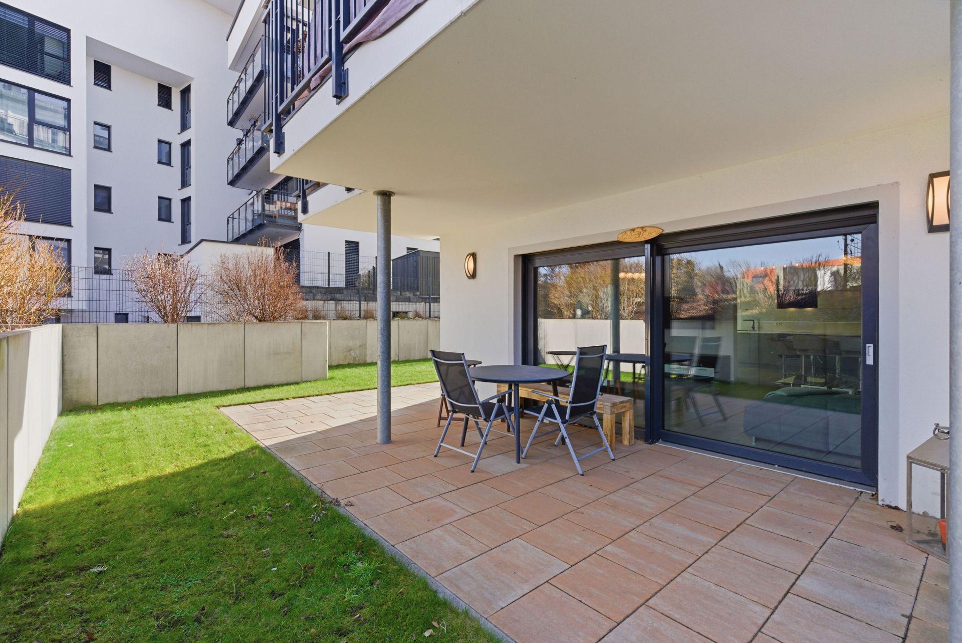Überdachte Terrasse mit Tisch und Stühlen, angrenzender Rasen und große Glas-Schiebetür.