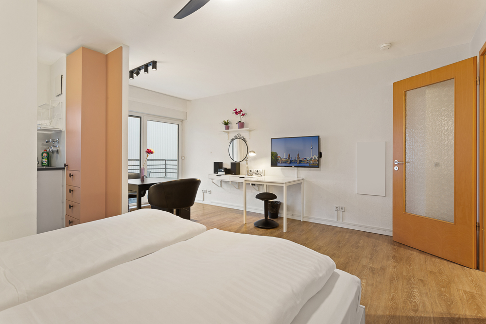 Modernes Schlafzimmer mit Doppelbett, Schreibtisch, Fernseher, Holzboden und Zugang zu einem Balkon.