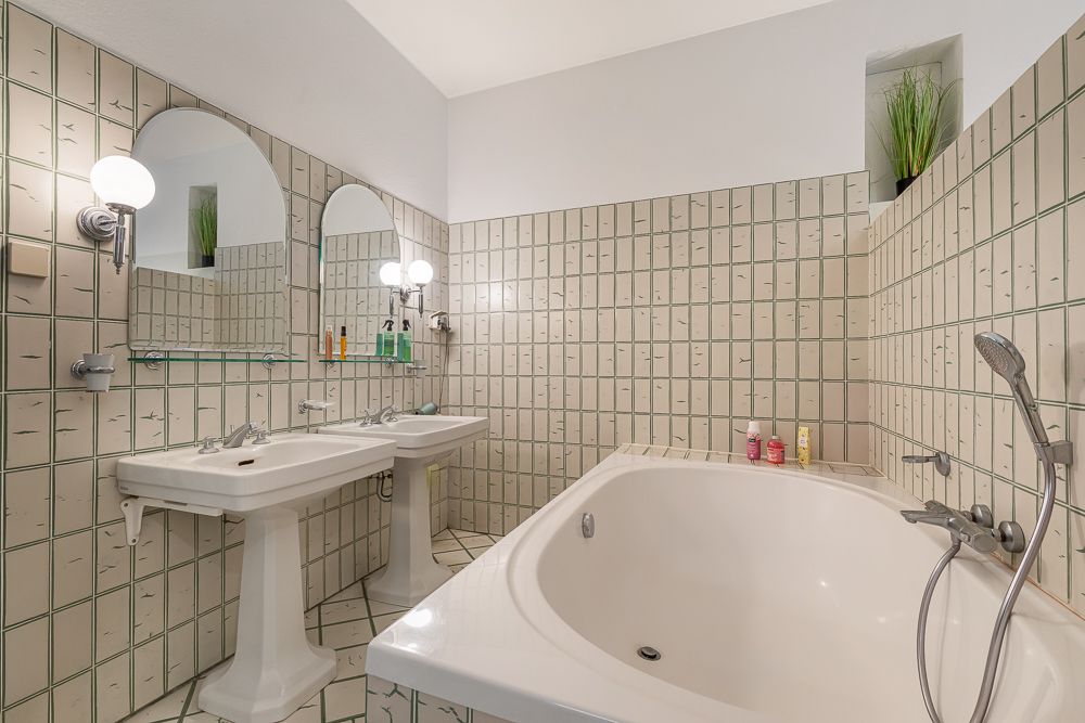 Badezimmer mit großer Badewanne, zwei Waschbecken, Spiegeln und Fliesenwänden.
