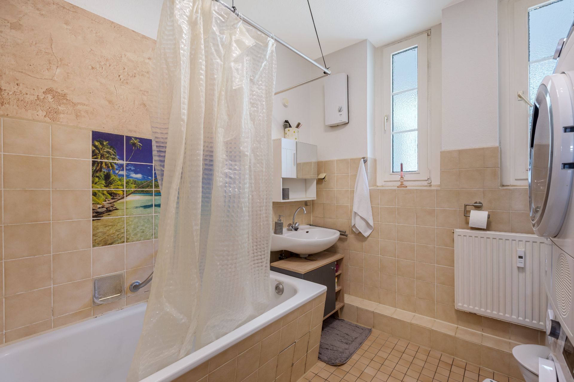 Helles Badezimmer mit Badewanne, Duschvorhang, Waschbecken, Waschmaschine und zwei Fenstern.