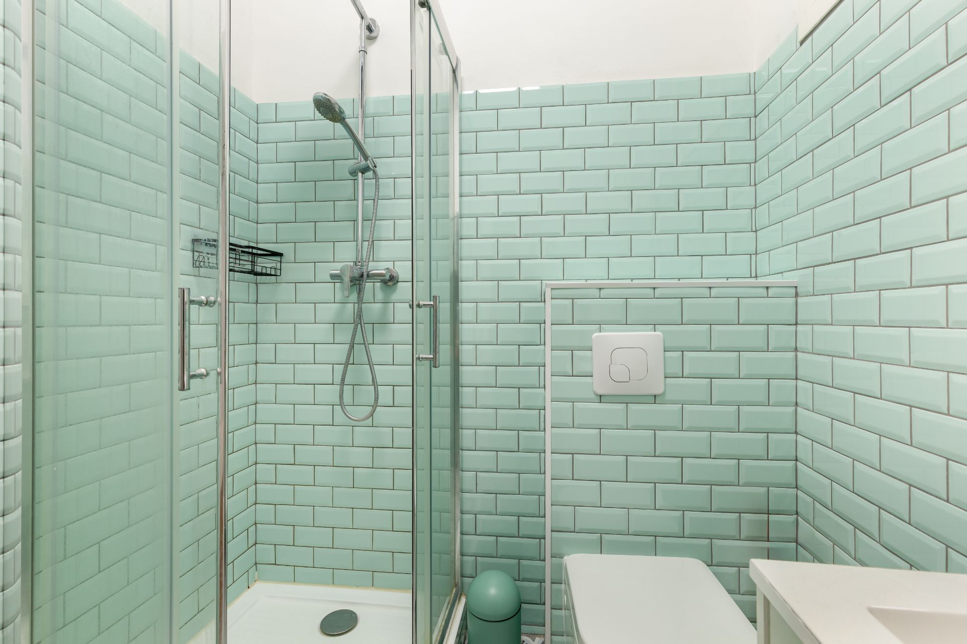 Modernes Bad mit Glasdusche, Toilette und mintgrünen Fliesen an den Wänden.