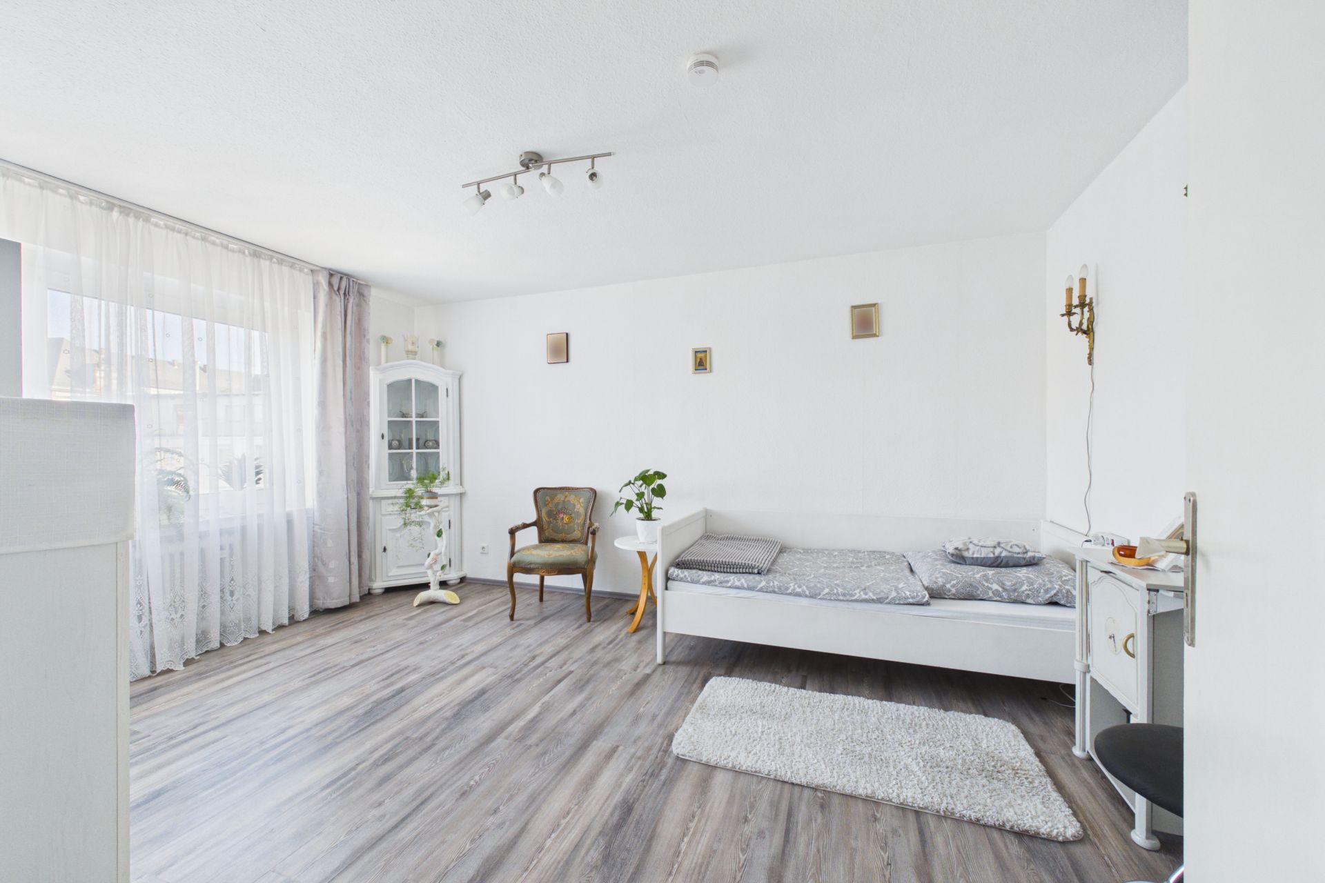 Helles Schlafzimmer mit Holzboden, Bett, Teppich, Sessel, Schrank und großem Fenster.