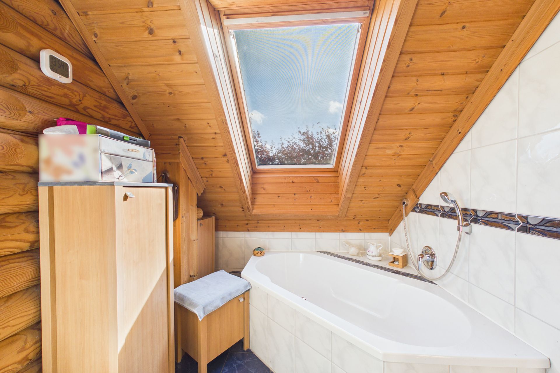 Badezimmer mit Badewanne unter Dachschräge, Holzdecke und großem Dachfenster.