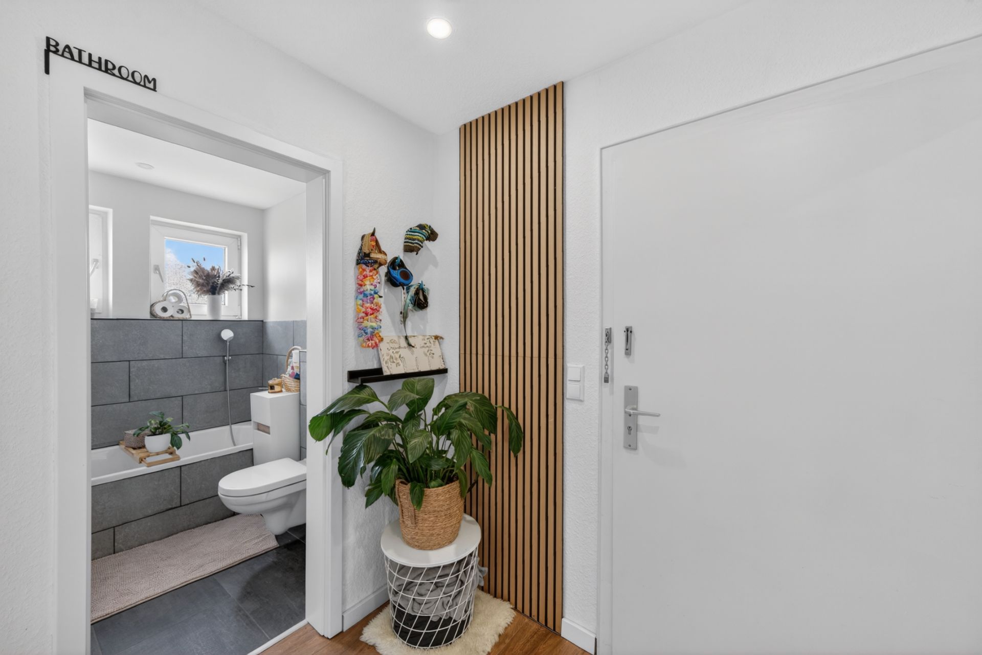 Eingangsbereich mit Zimmerpflanze, Blick ins Badezimmer mit Toilette und Badewanne.