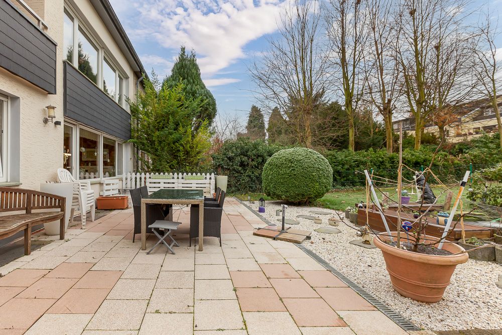 Große Terrasse mit Sitzmöbeln, Garten und verschiedenen Pflanzgefäßen an einem Wohnhaus.