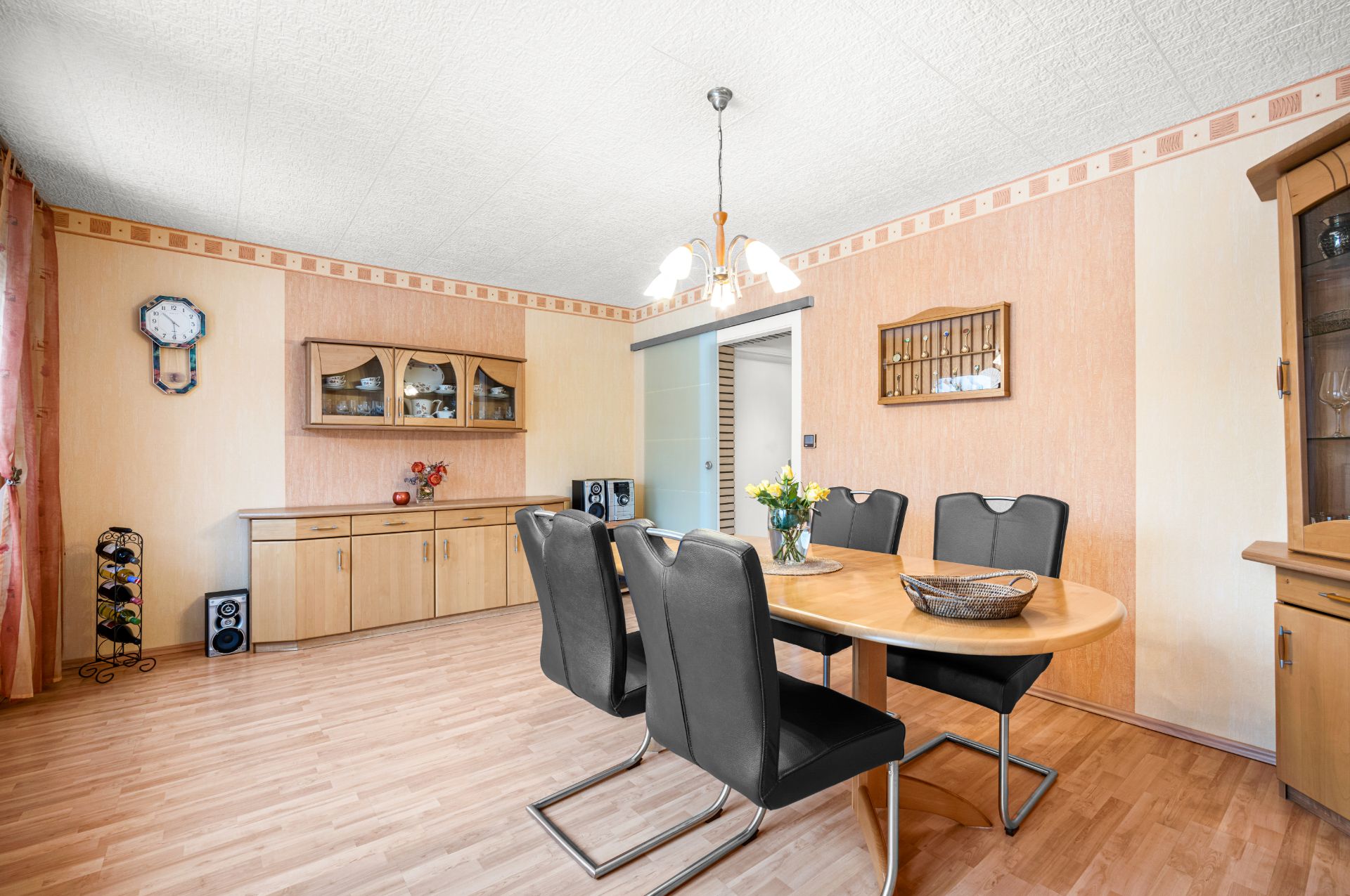 Esszimmer mit rundem Holztisch, vier schwarzen Stühlen und Sideboard an der Wand.