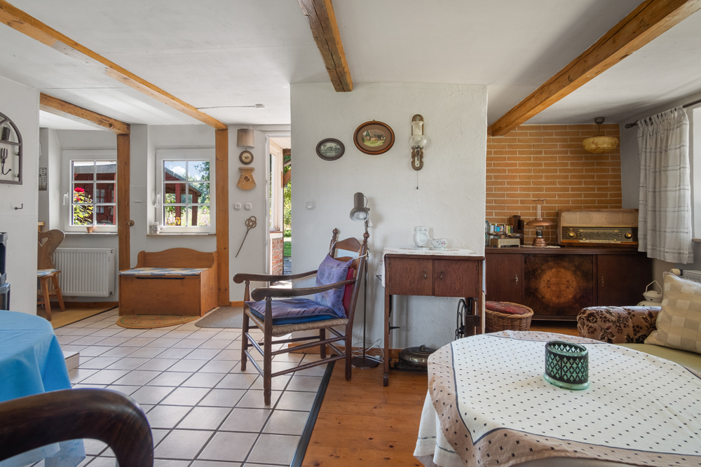 Gemütliches Wohnzimmer mit Holzbalken, Vintage-Möbeln, Sessel und Blick auf Küche und Garten.