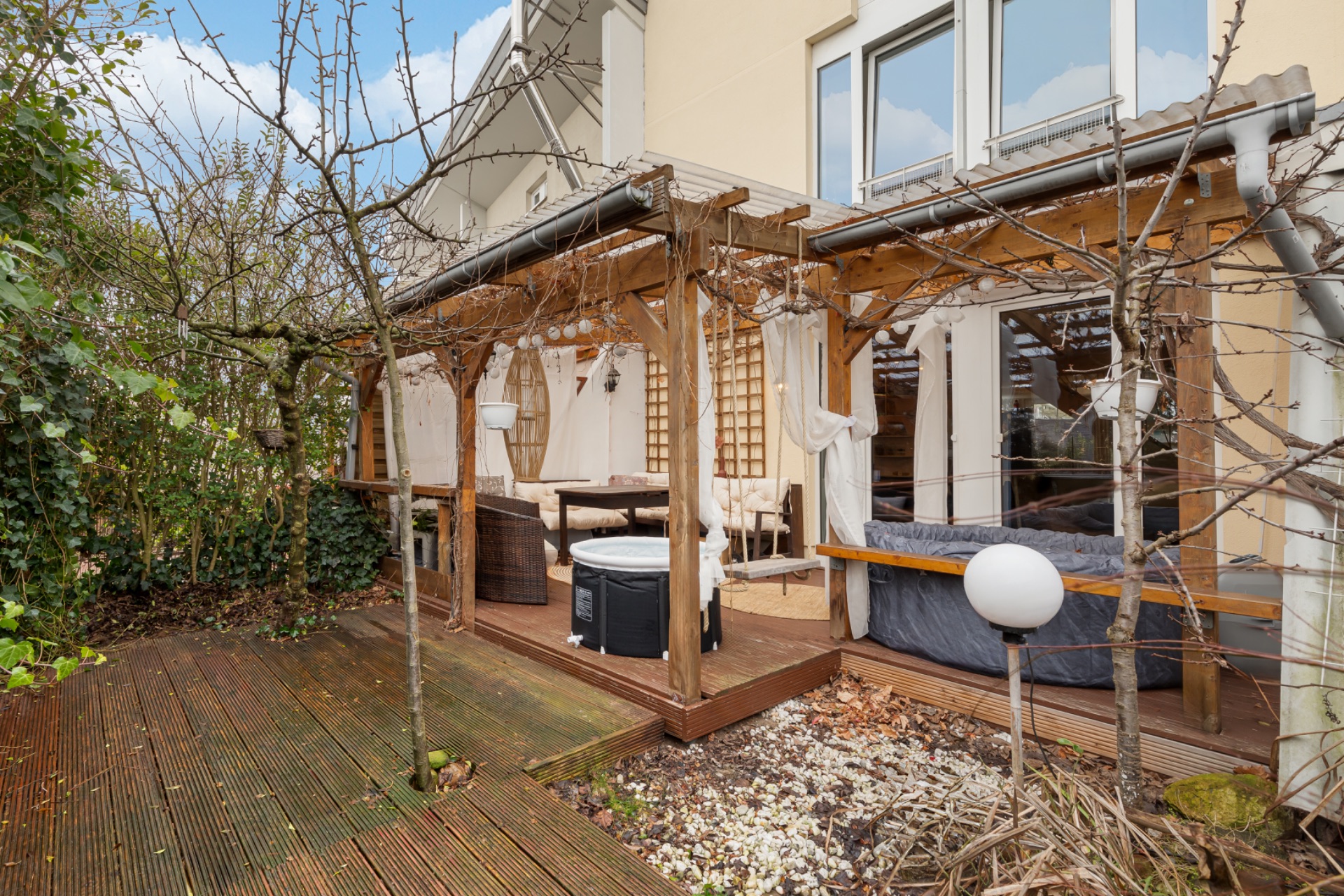 Holzterrasse mit Pergola, Gartenmöbeln und Whirlpool im Garten eines Wohnhauses.