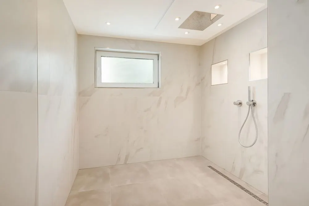 Große, moderne begehbare Dusche mit Marmorfliesen, Fenster und eingelassener Regendusche.