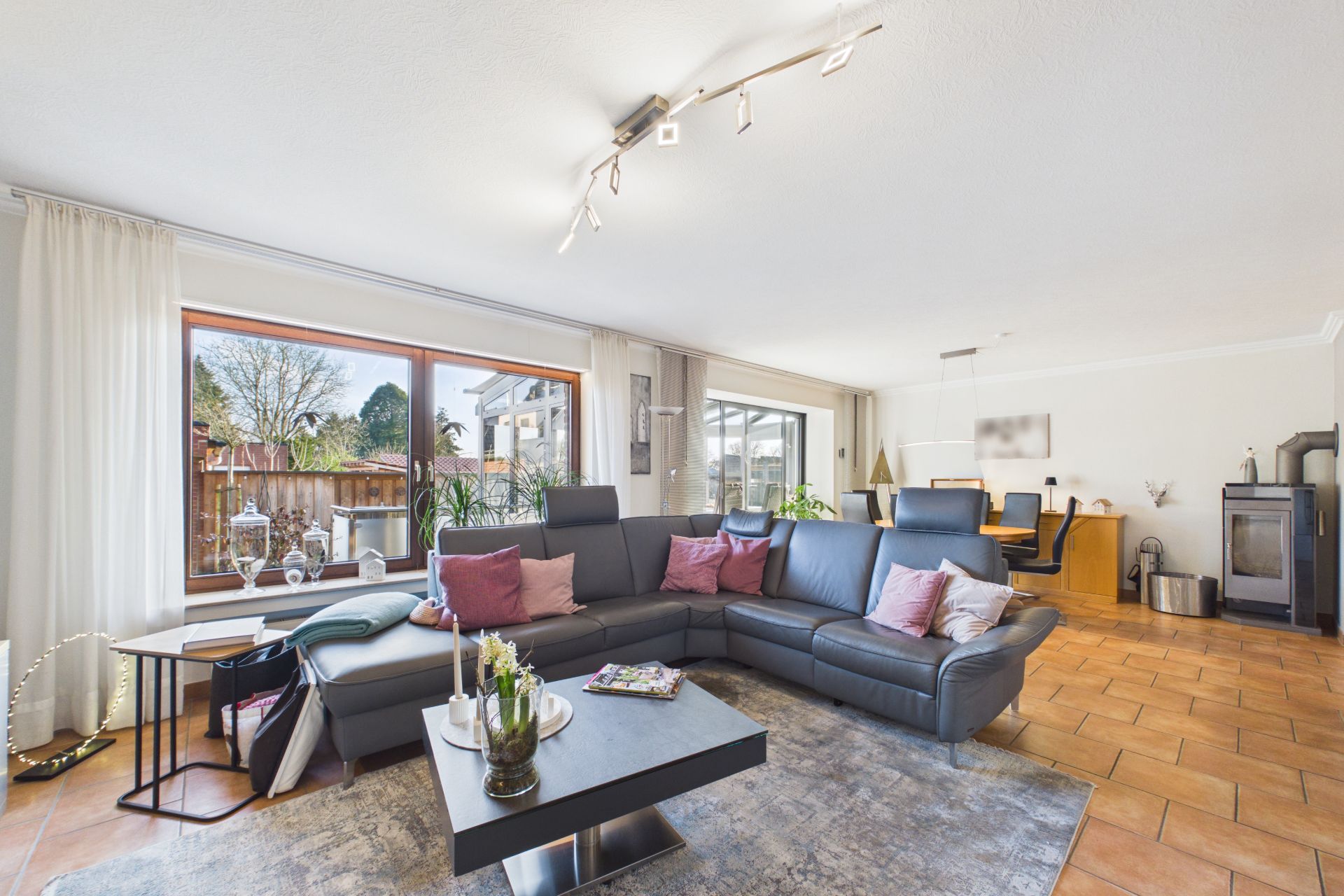 Helles Wohnzimmer mit großer Eckcouch, Couchtisch, Kamin und Essbereich im Hintergrund.
