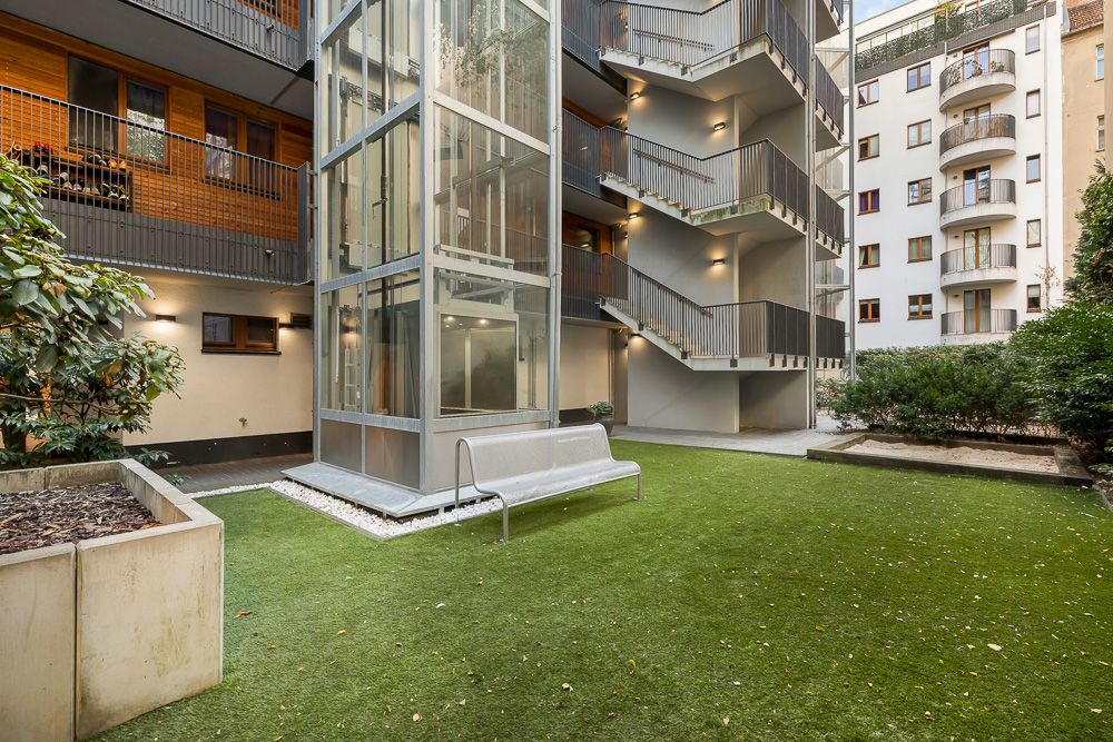 Innenhof mit Glasaufzug, Sitzbank, Kunstgras und umliegenden Wohnungen.
