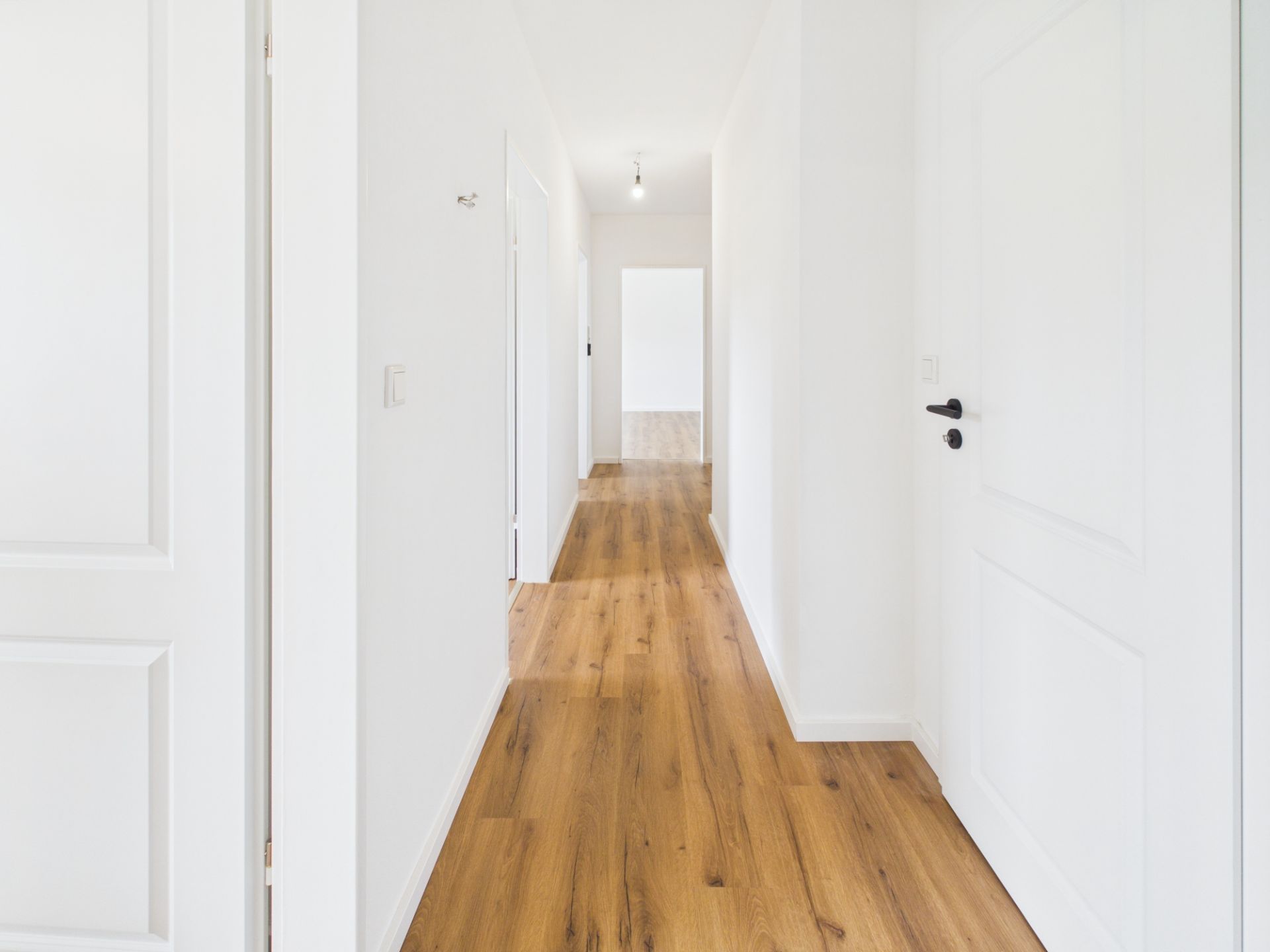 Heller Flur mit weiß gestrichenen Wänden und Holzfußboden, mehrere weiße Türen seitlich.