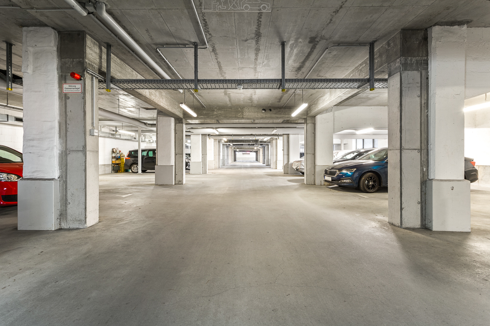 Innenansicht einer Tiefgarage mit mehreren geparkten Autos und Betonsäulen.