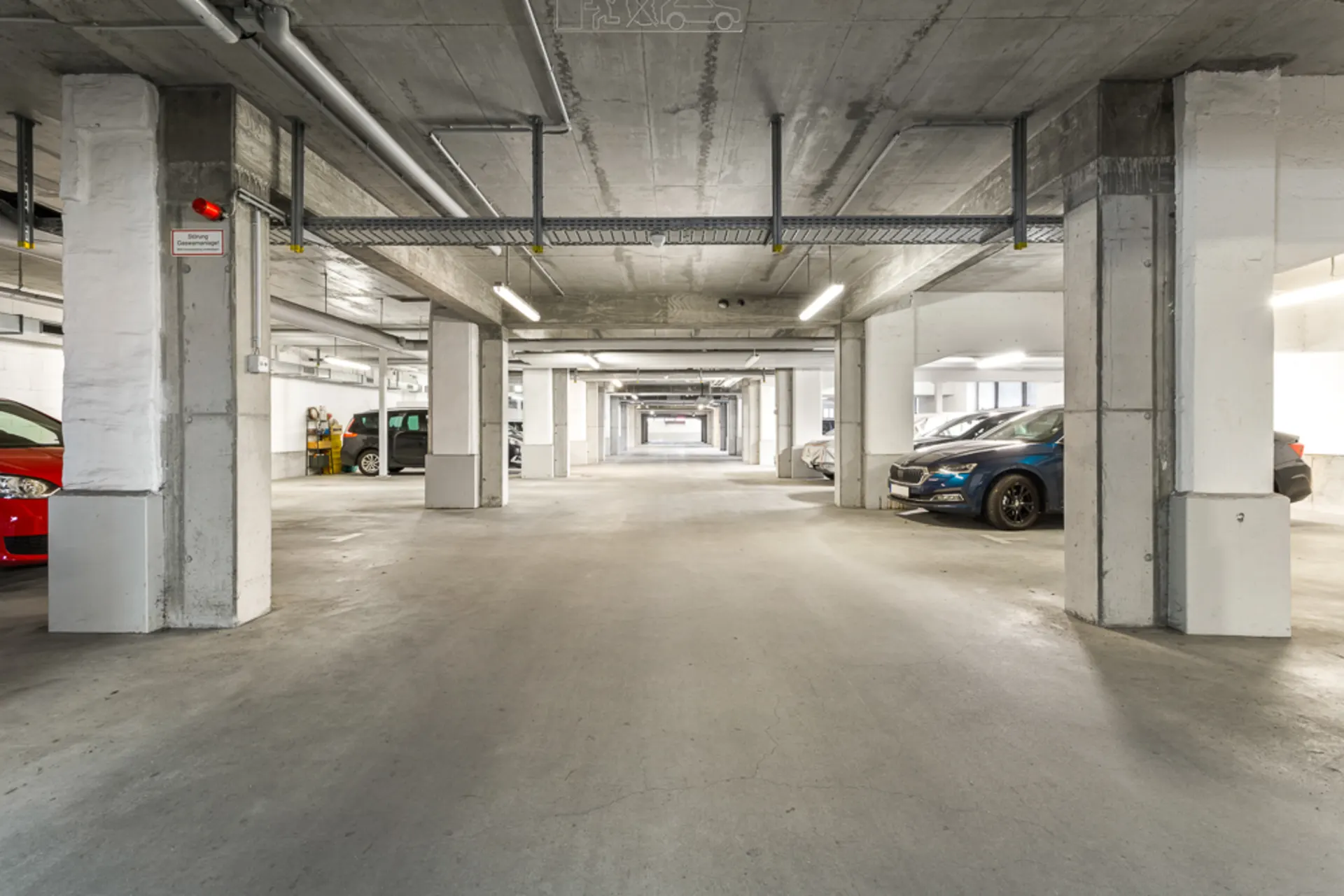 Innenansicht einer Tiefgarage mit mehreren geparkten Autos und Betonsäulen.