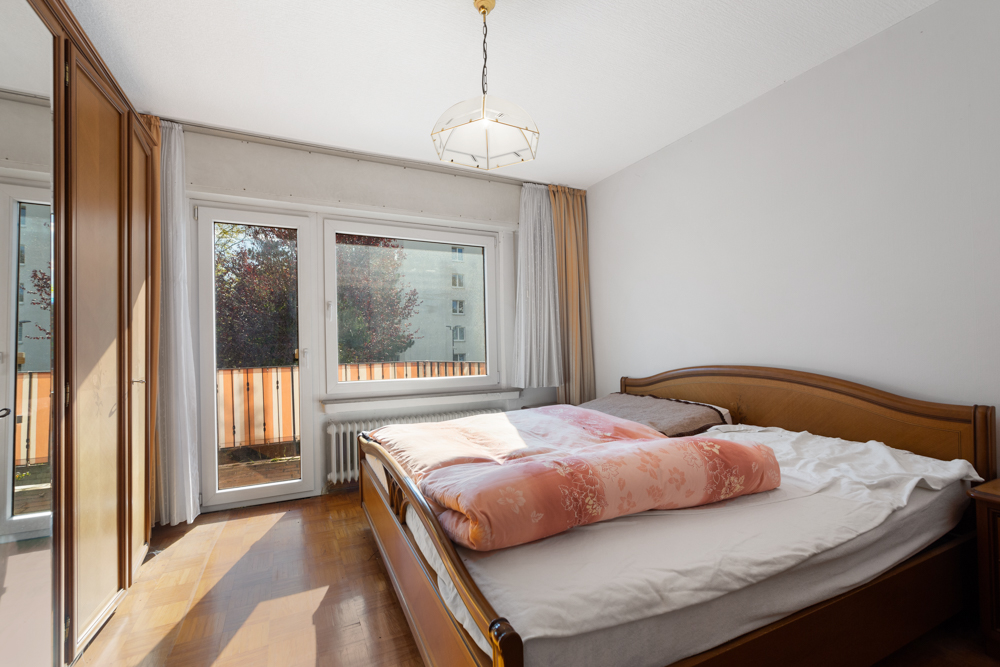 Helles Schlafzimmer mit großem Bett, Holzschrank und Zugang zu einem Balkon.