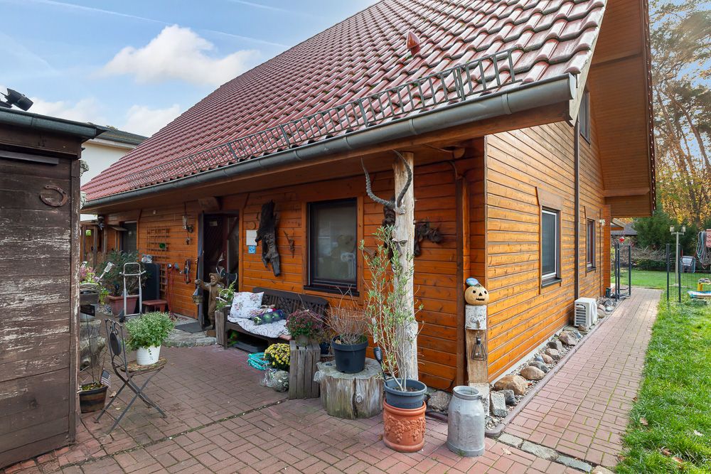 Einfamilienhaus mit Holzfassade, rotem Dach und bepflanztem Eingangsbereich.