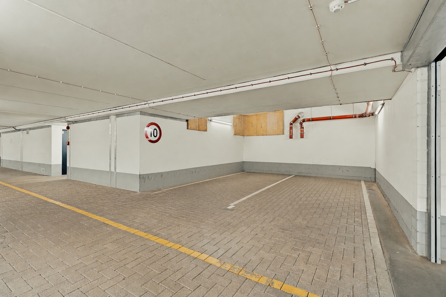 Leerer Tiefgaragenstellplatz mit gelber Linie und Verkehrsschild für 10 km/h an der Wand.