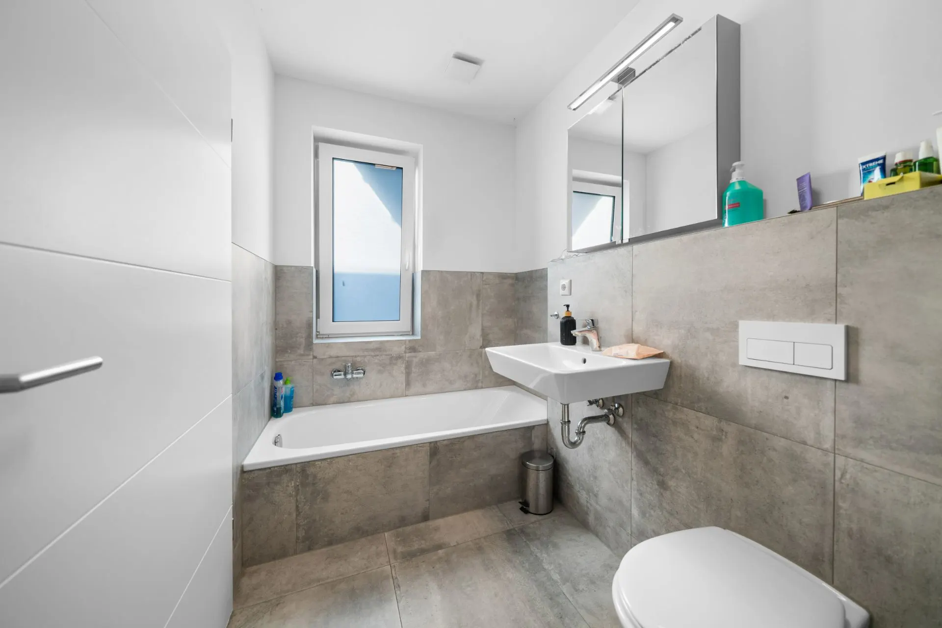 Modernes Badezimmer mit Badewanne, Waschbecken, Spiegel und Fenster.