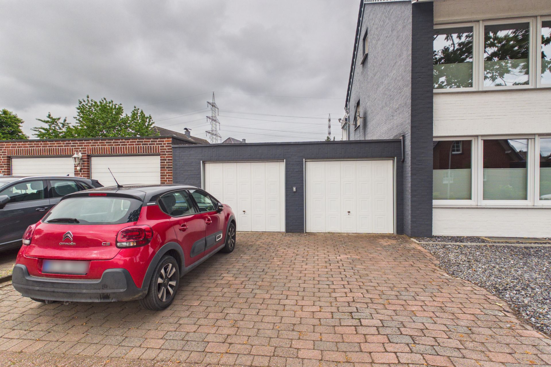 Roter Pkw steht auf gepflasterter Einfahrt vor Doppelgarage an Wohnhaus.