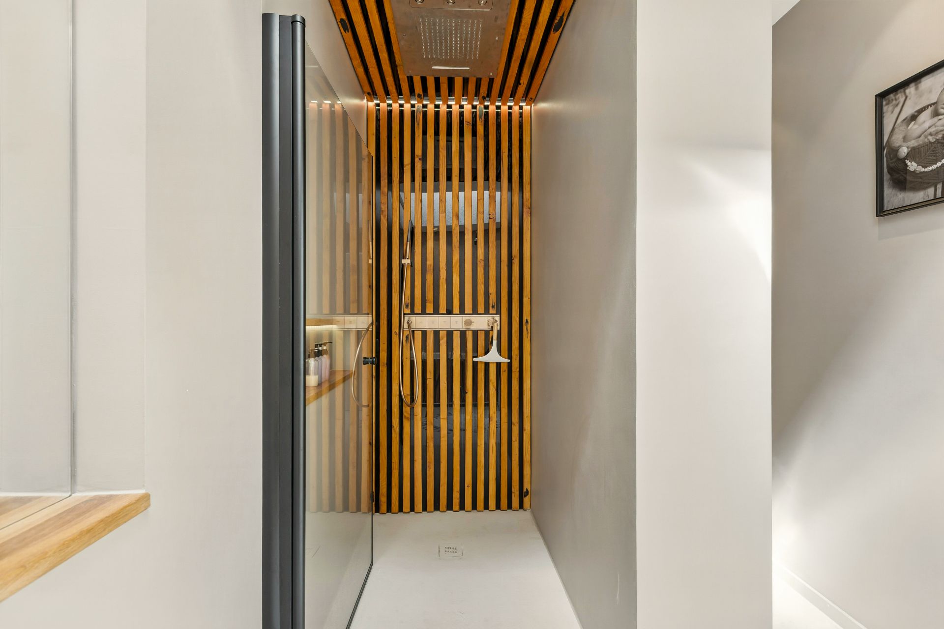 Moderne Dusche mit Holzelementen an Wand und Decke, Glasabtrennung, helles Licht.