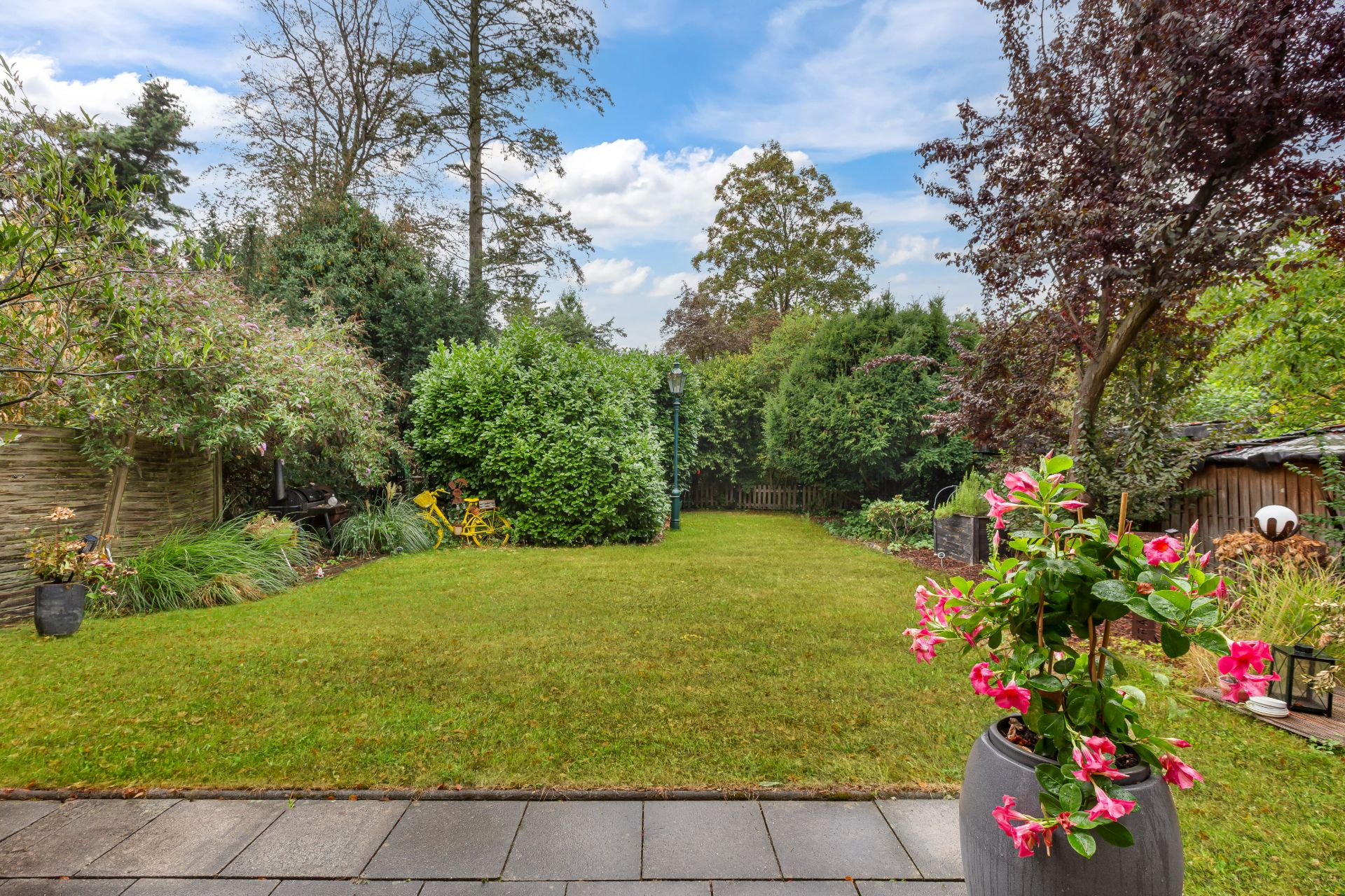 Gepflegter Garten mit Rasenfläche, Blumen, Bäumen und Terrasse im Vordergrund.