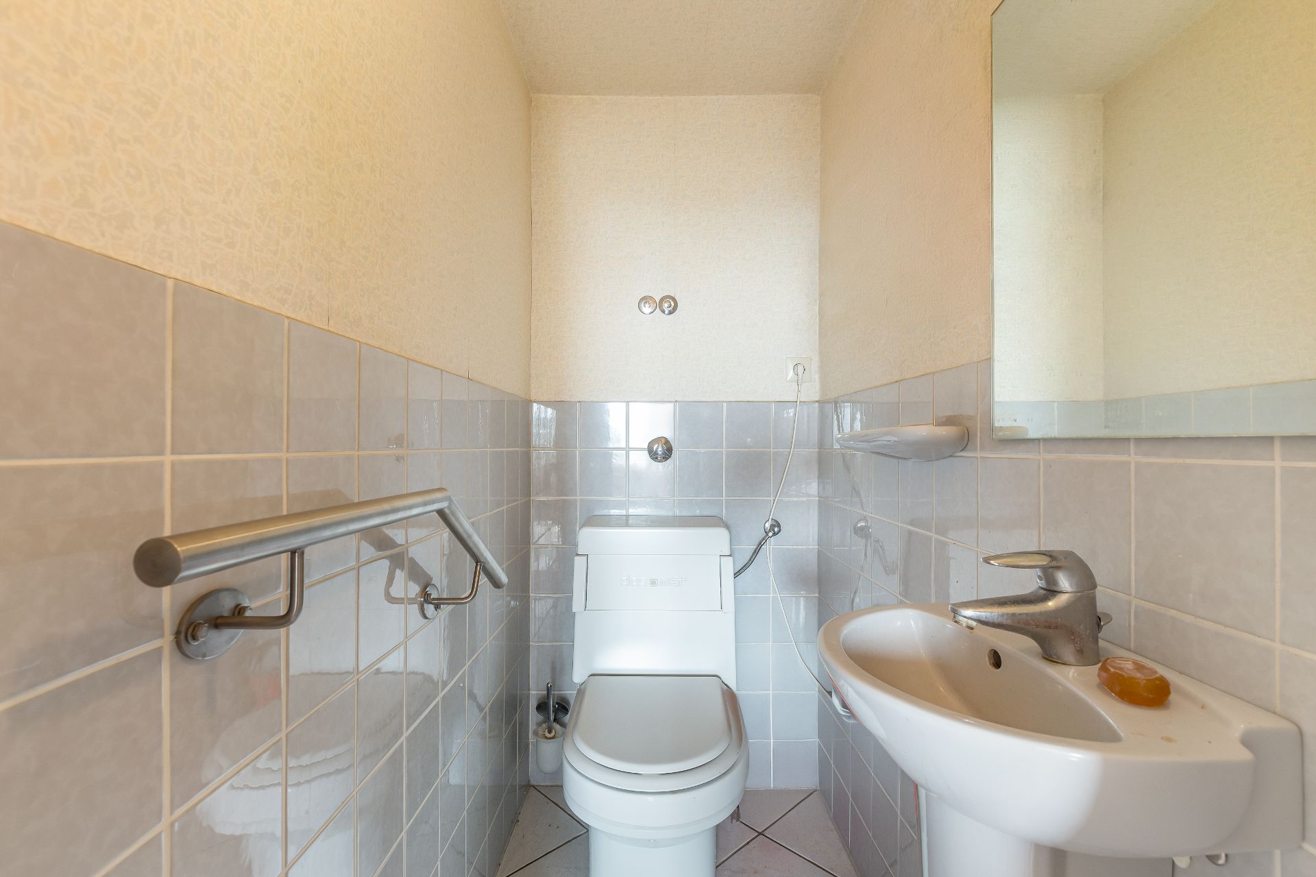 Kleines Badezimmer mit Toilette, Waschbecken, Haltegriff und Spiegel an der Wand.